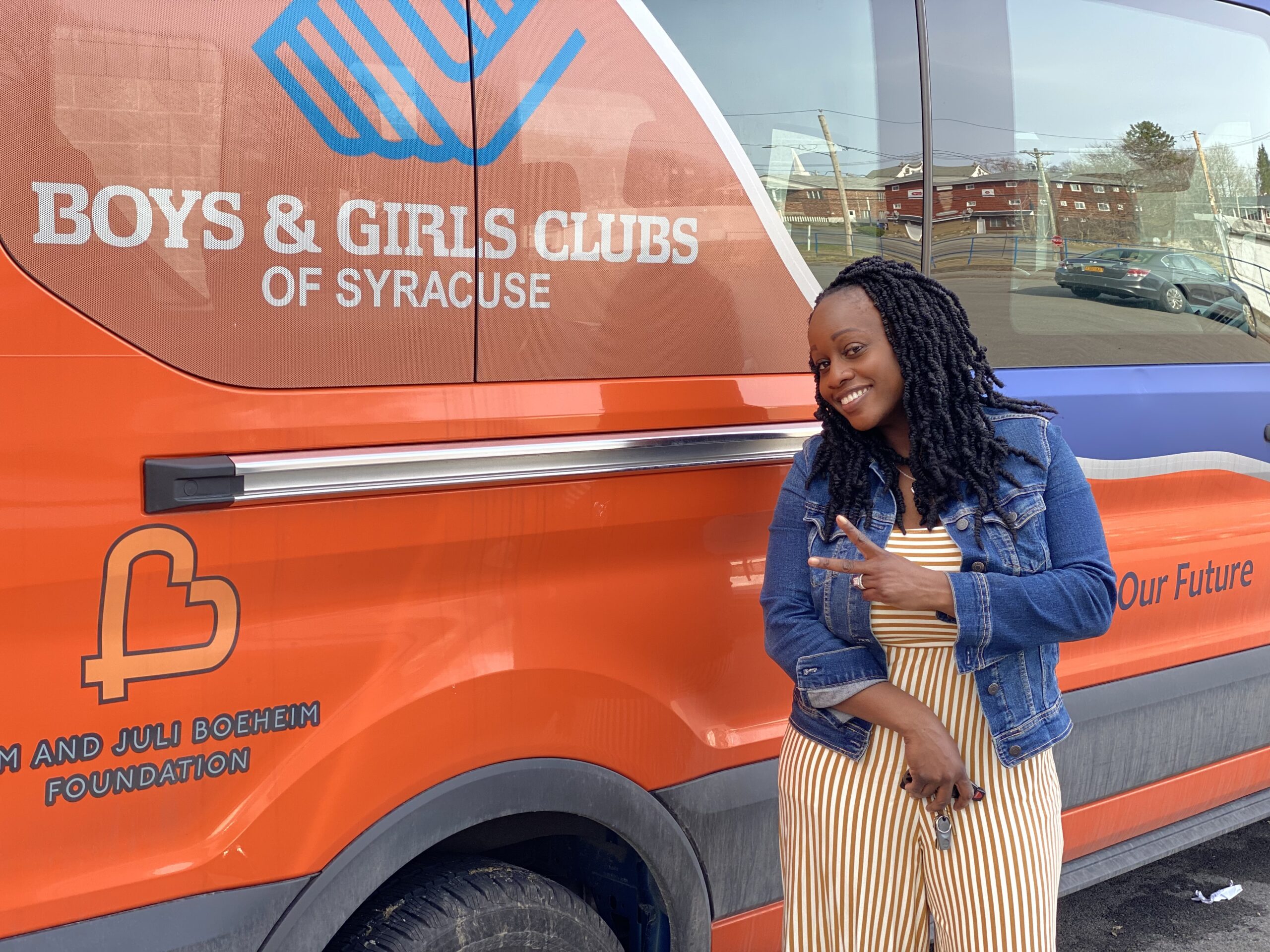 African American Woman standing in front of a blue and orange colored Boys & Girls Club Truck